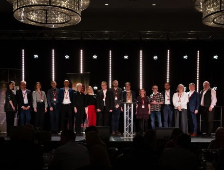 16 people stood in a line on stage, smiling