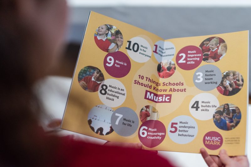 Over the top of someone's shoulder (blurred) is a clear view of the booklet '10 things schools should know about Music'