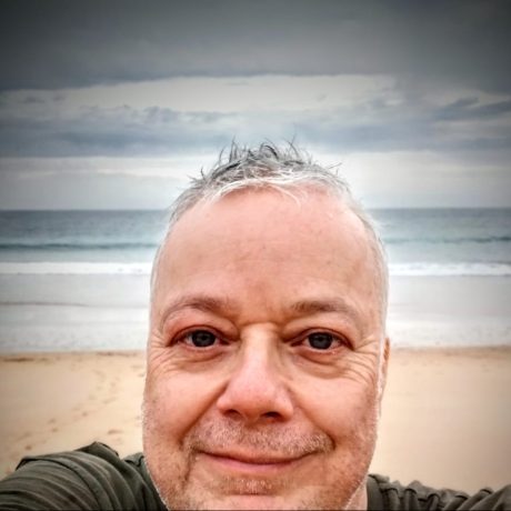Dan Somogyi smiling at the camera with the beach and sea in the background.