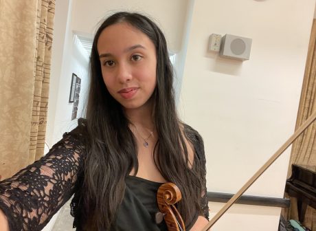 Danya has long dark hair and is wearing a black top. 