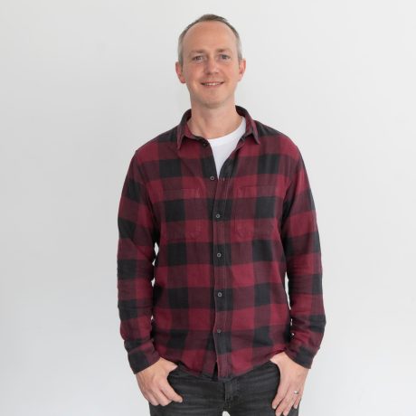 David is wearing a red and black plaid shirt. He is smiling at the camera.