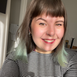 Elen has shoulder length brown hair with a blue ombre at the bottom. She is smiling and is wearing a stripy top.