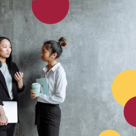Two people having a conversation in work clothes, in front of a grey wall.