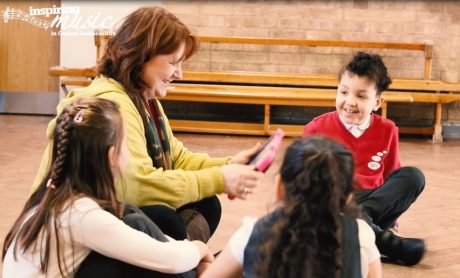 A teacher is sat on the floor with three pupils holding an iPad.