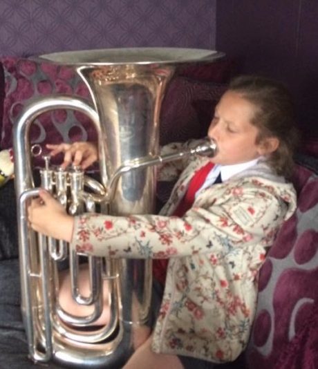 Holly as a child playing the tuba, sat down.