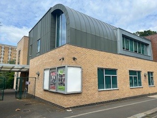 The outside of Hounslow Music Centre, with pale bricks on the lower half and a grey curved roof