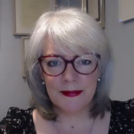 Lucy Reid is wearing a black and white blouse and glasses.