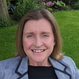 Woman in blazer in front of grass background.