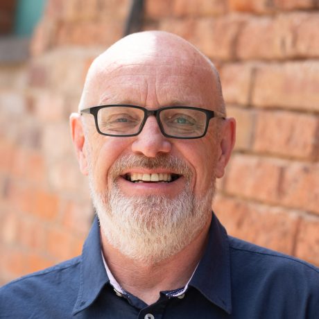 Man smiling directly towards camera in blue shirt.