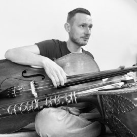 Pete Yelding holding cello with Sitar in foreground