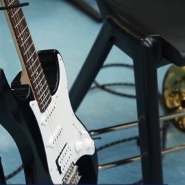 An electric guitar on a stand and a trombone under a chair in a classroom