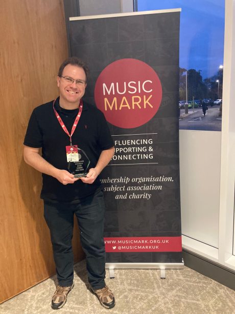 Scott standing next to a Music Mark banner holding a glass award