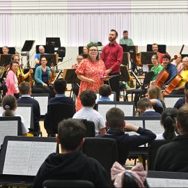 Young People watch a orchestra as conductor smiles facing them.