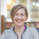 Diana Salazar smiling at the camera. She has short, light hair and is wearing a grey blazer.