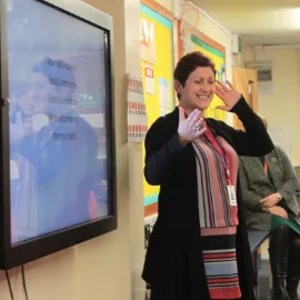 A music teacher stands in front of a digital whiteboard.