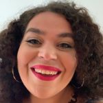 Hannah Thuraisingam Robbins smiling at the camera. She has dark curly hair and pink lipstick.