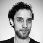 James Prosser smiling at the camera in black and white. He has short curly hair and a short beard.