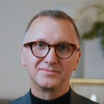 Michael Price looking at the camera. He has short dark hair and round framed glasses