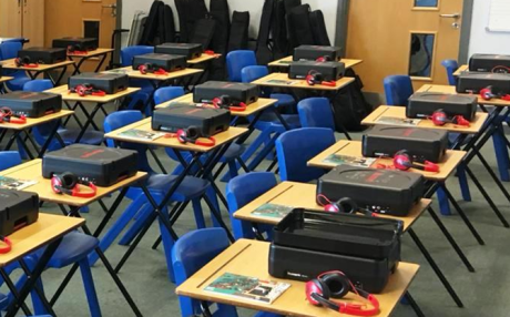 Music technology packs laid out on individual school desks in rows with blue chairs at each desk