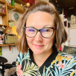 Rachael Perrin smiling at the camera. She has short brown hair and glasses, and a patterned top.