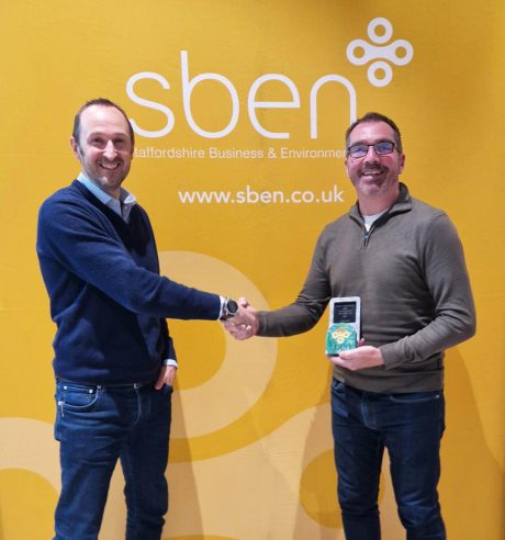 Two men shaking hands, one holding an award in front of a yellow banner reading 'SBEN'