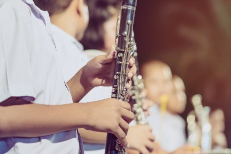Hands on a clarinet, with blurred background of other young people holding instruments.