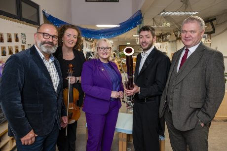 A group of five adults smiling at the camera, one woman holding a violin and one man holding a bassoon