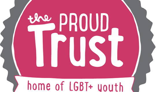 Pink circle with white text reading 'The Proud Trust' surrounded by a grey circle with spikes. White banner across the front with pink text reading 'Home of LGBT+ youth'
